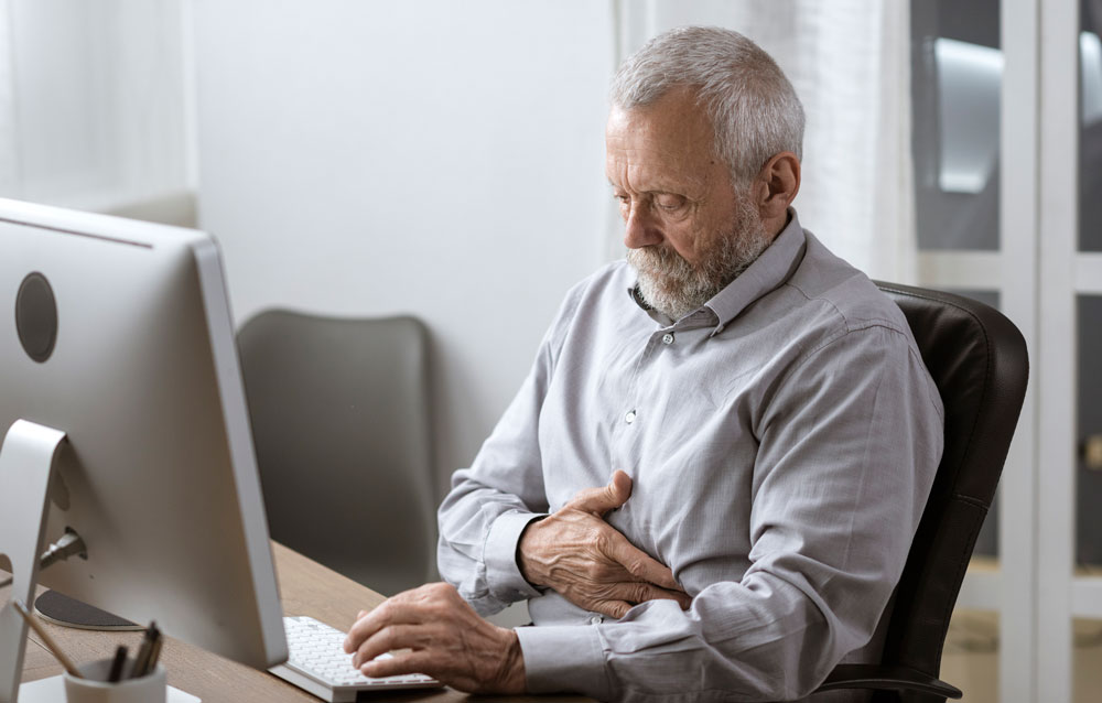 old man holding his stomach while facing his computer