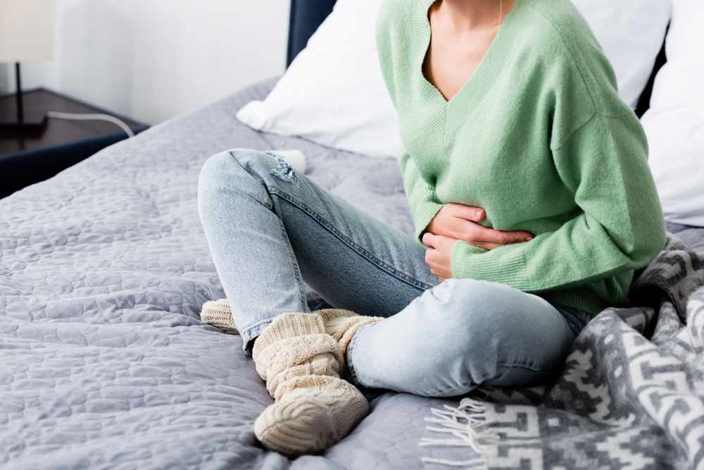 female sitting on her bed with her hands on her stomach