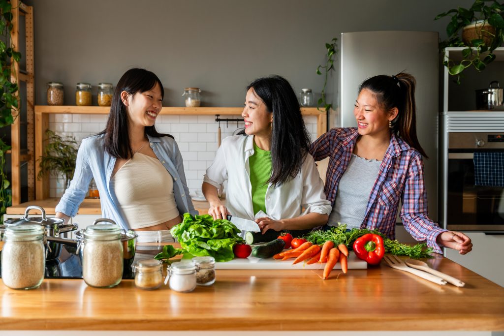 three young women standing with a table full of fruits and vegetables